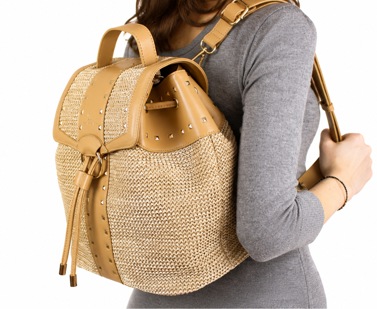 A woven straw backpack with tan leather trim, studded details, and a top handle, shown against a plain white background.