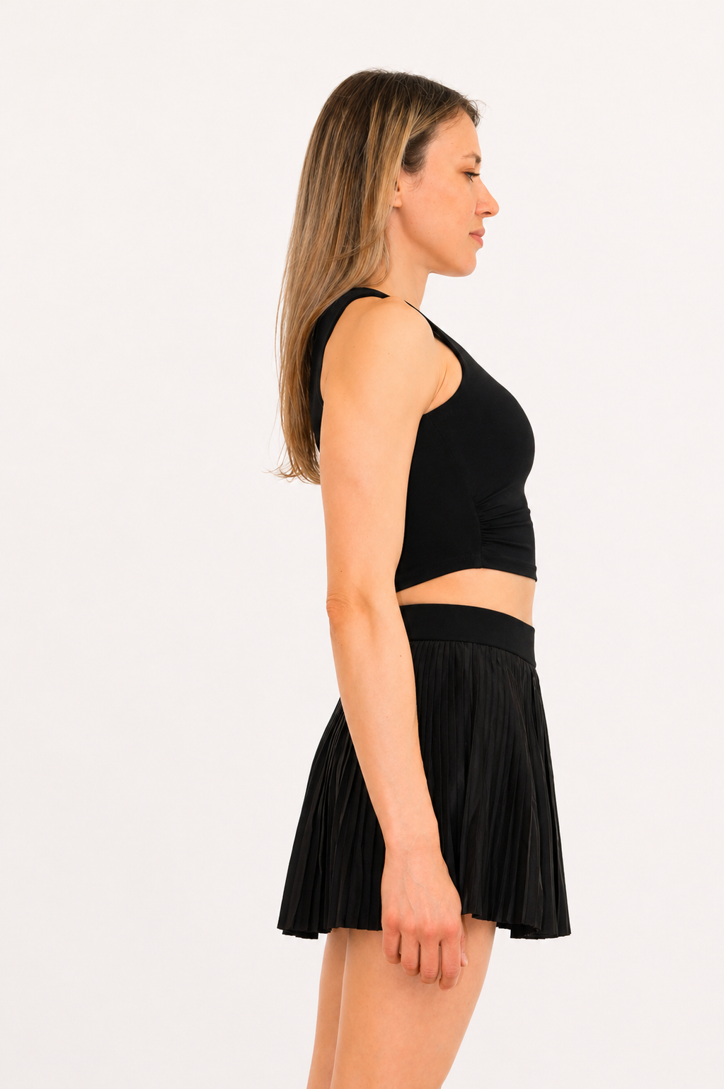 Woman wearing a black sleeveless top and pleated skirt on a white background